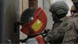 Soldier equipped with saw cuts through steel door.