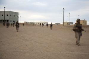 Soldiers patrol through open terrain at the edge of a town